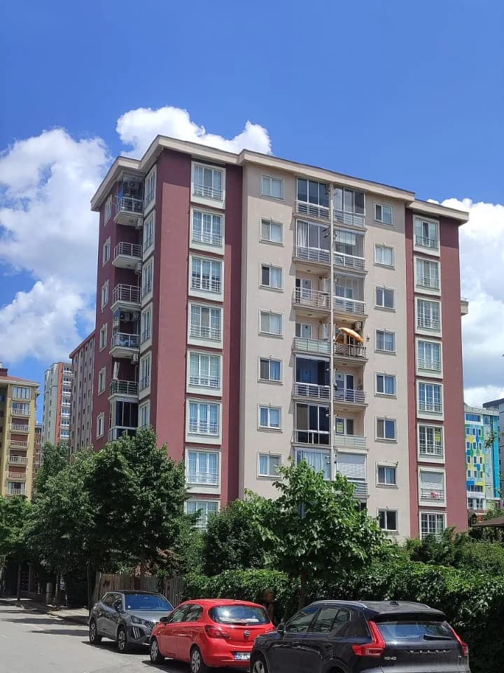 Apartmanın açılı görünüşü; yan cephedeki balkonlar, arkada beyaz bulutlar.