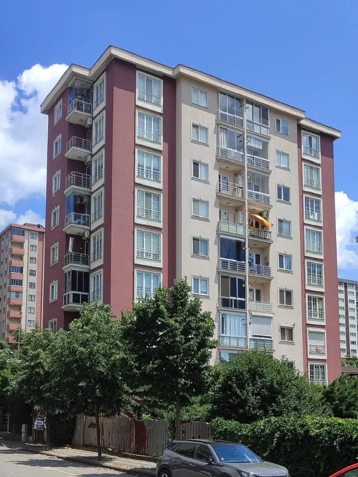 Köşeden görünüş: yan cephe balkonları ve bordo köşe şeridi.