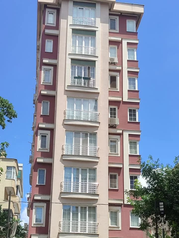 Apartmanın en üst katları ve saçak çizgisi, açık mavi gökyüzü önünde.
