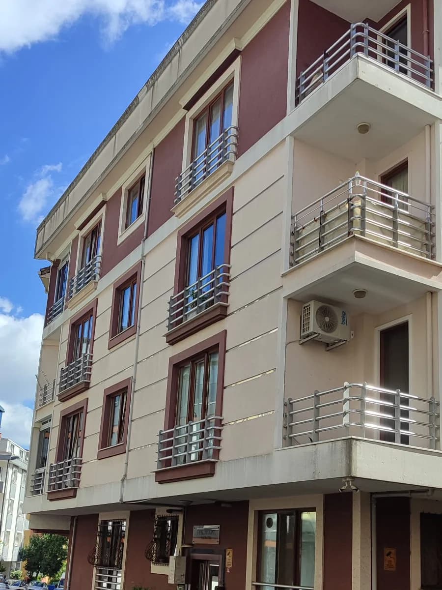 Köşeden aşağıdan bakış: bordo pencere çerçeveleri ve metal korkuluklu balkonlar.
